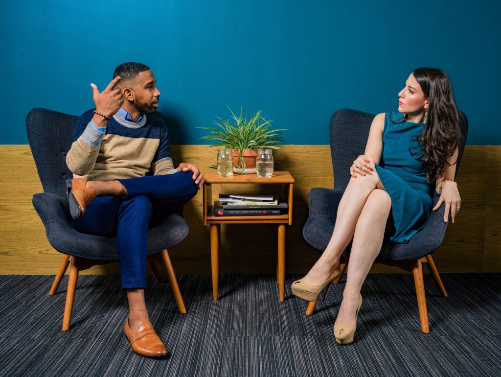 woman-wearing-teal-dress-sitting-on-chair-talking-to-man-2422280