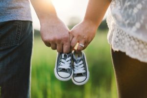 Mommy and daddy holding hands and little baby shoes.