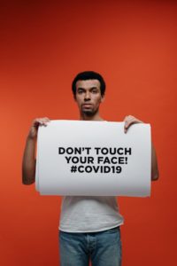 A guy holding a sign that says not to touch your face because of the coronavirus outbreak. After moving out of your LA music studio you could try to help spread the word about the proper way to do so.