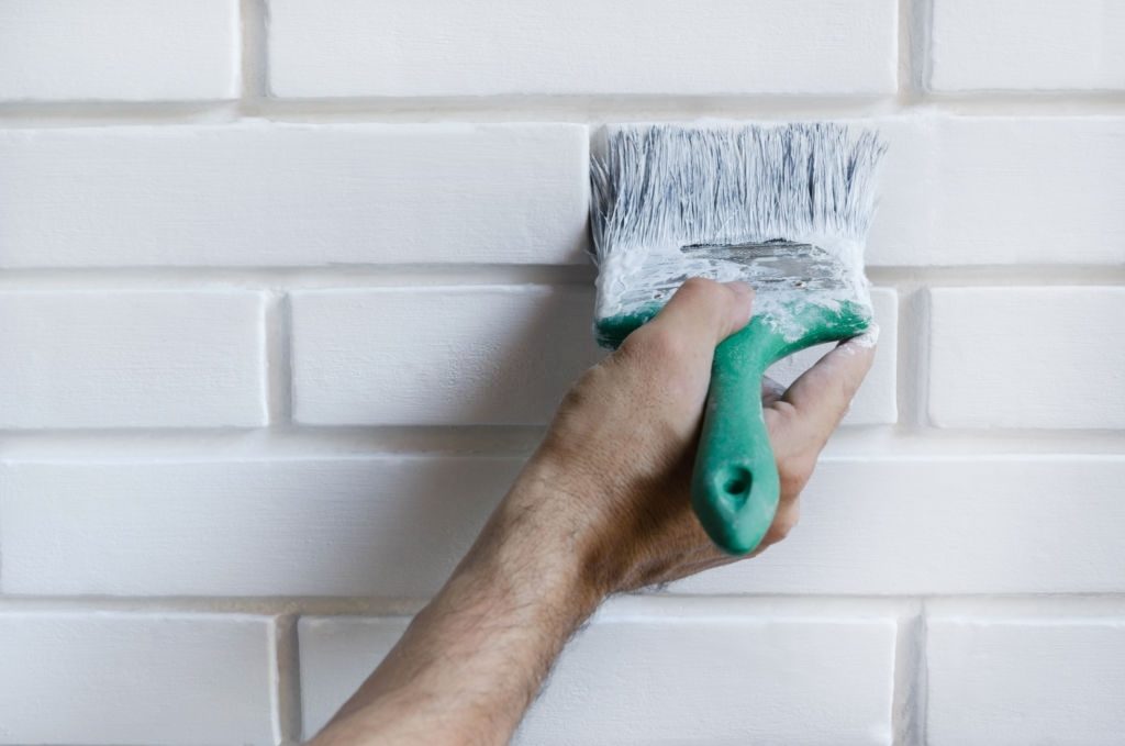 Man painting with brush brick wall on white color, close-up